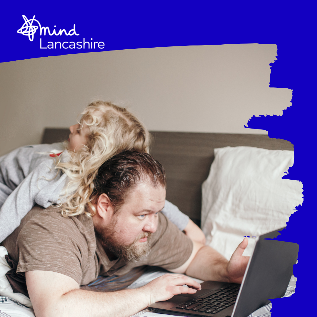 Dad lying on a bed trying to work on laptop with his young daughter lying on his back.